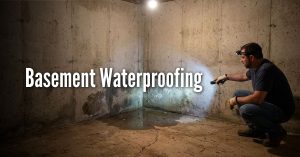 An image titled "Basement Waterproofing" showing a man inspecting a damp residential basement. He is wearing a dark t-shirt, jeans, work gloves, and a headlamp, and he is crouching down to point a flashlight at a corner where the concrete walls and floor meet. The walls show visible dark water stains and dampness, and there is a small pool of standing water on the cracked concrete floor. Identifying the source of the leak—whether it's hydrostatic pressure from the soil or a simple crack—is the first step in choosing between interior sealants or exterior drainage solutions.