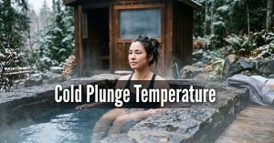 An image titled "Cold Plunge Temperature" featuring a woman sitting in a modern, black outdoor cold plunge tub. She is submerged up to her shoulders, wearing a black swimsuit and a focused expression. A white circular thermometer floats in the clear water next to her. The setting is a peaceful backyard with a wooden deck and green foliage in the background. Finding your ideal temperature "sweet spot"—usually between 10°C and 15°C (50°F and 60°F)—is key to consistent practice