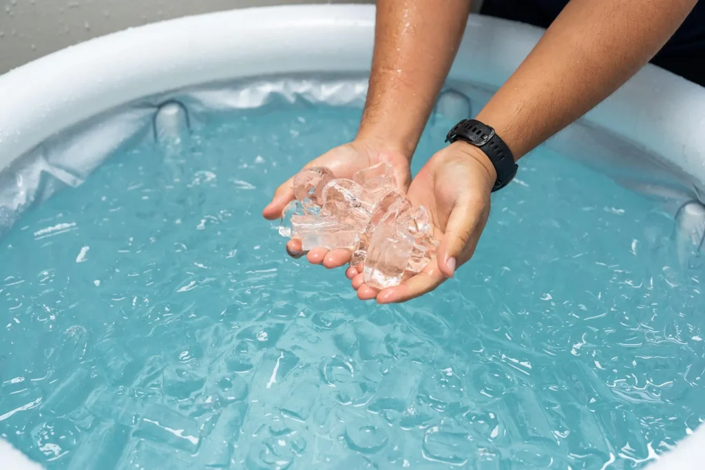 Close-up of a person holding ice cubes over a portable white inflatable ice bath tub filled with cold water.